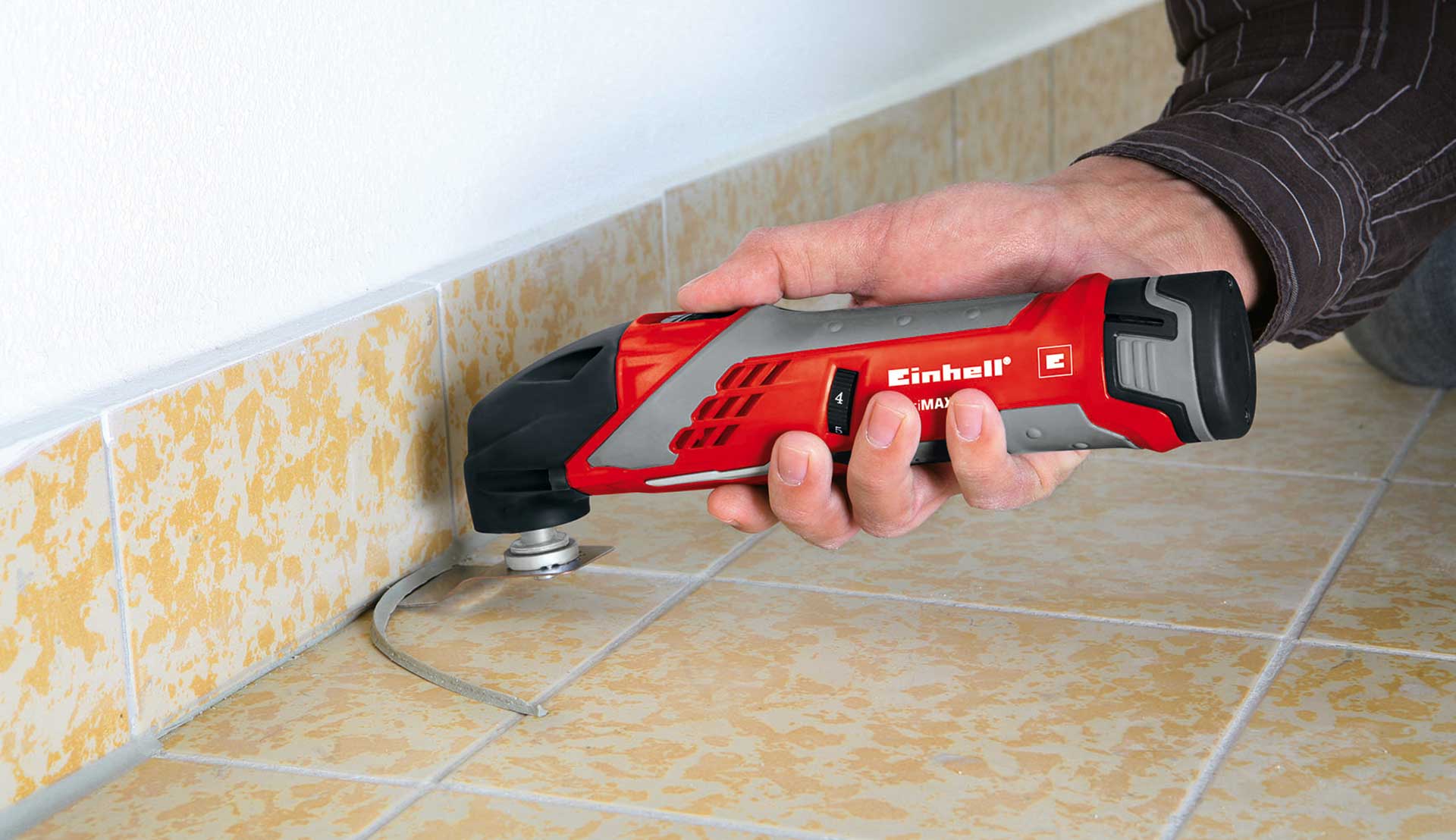 A hand holding a multifunction tool with a scraper attachment to remove an old silicone sealant.
