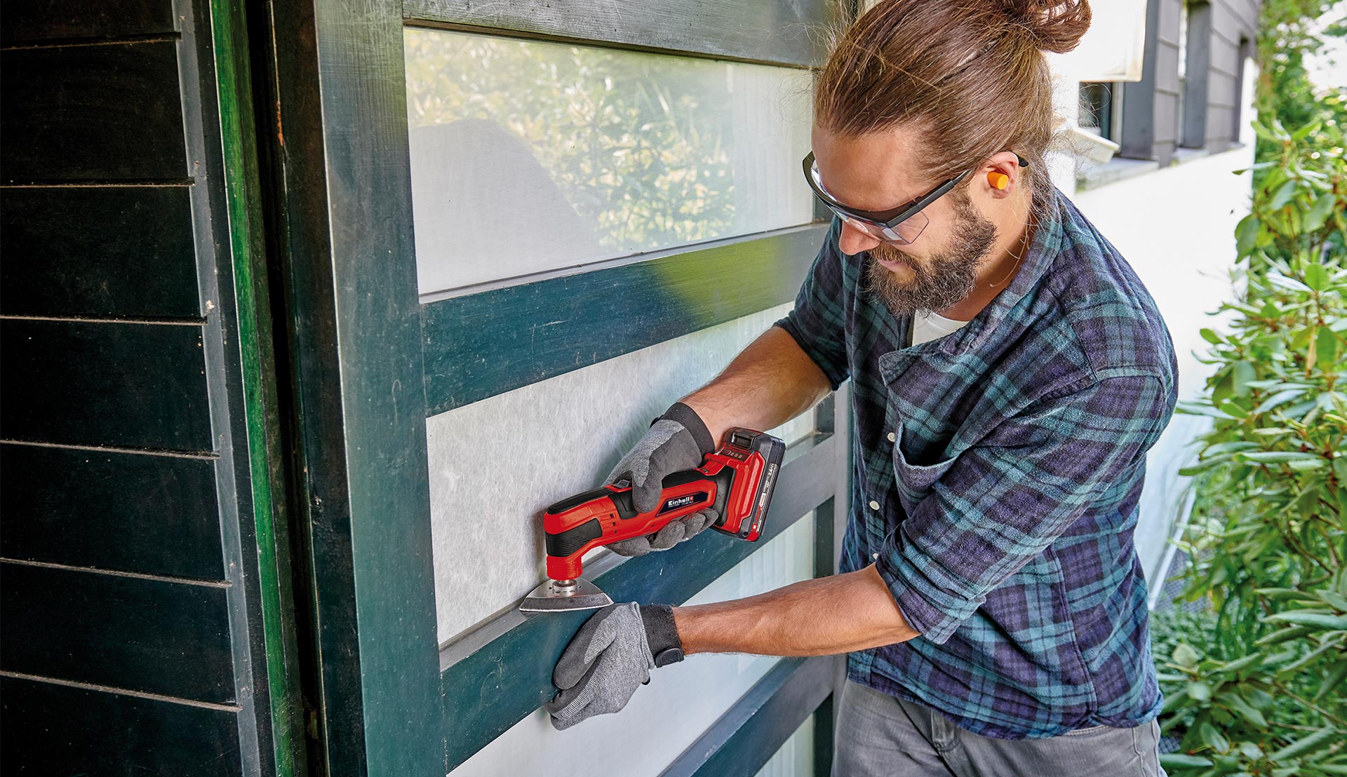 Man sanding narrow wooden surface on a door with a multifunctional tool.