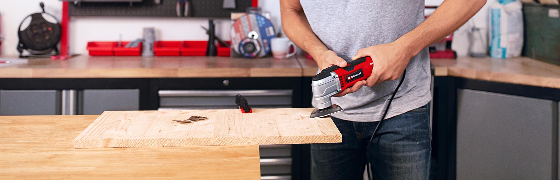Ein Mann in seiner Werkstatt bearbeitet eine Holzplatte mit einem Multifunktionswerkzeug.