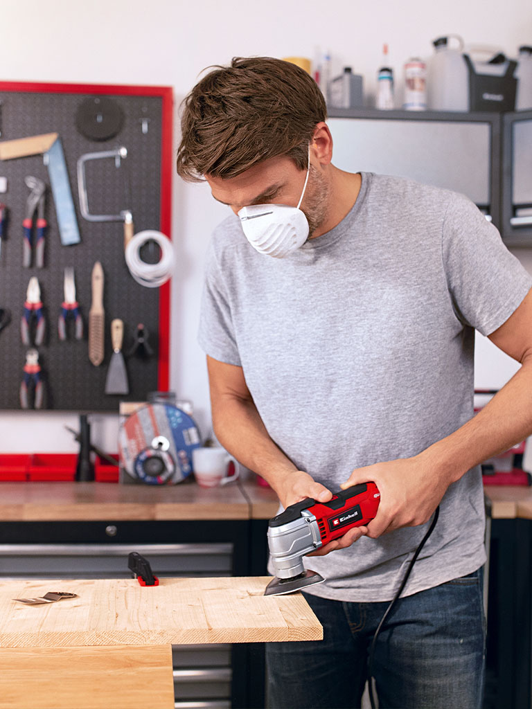 Ein Mann schleift in seiner Werkstatt mit dem Einhell Multifunktionstool ein Holzbrett.