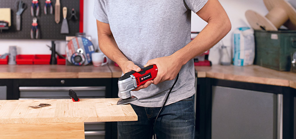 Ein Mann schleift in seiner Werkstatt mit dem Einhell Multifunktionstool ein Holzbrett.