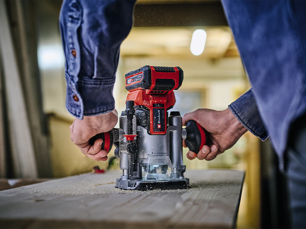 Close-up of two men's hands milling into a wooden panel with the Einhell TP-RO 18 Li BL cordless router.