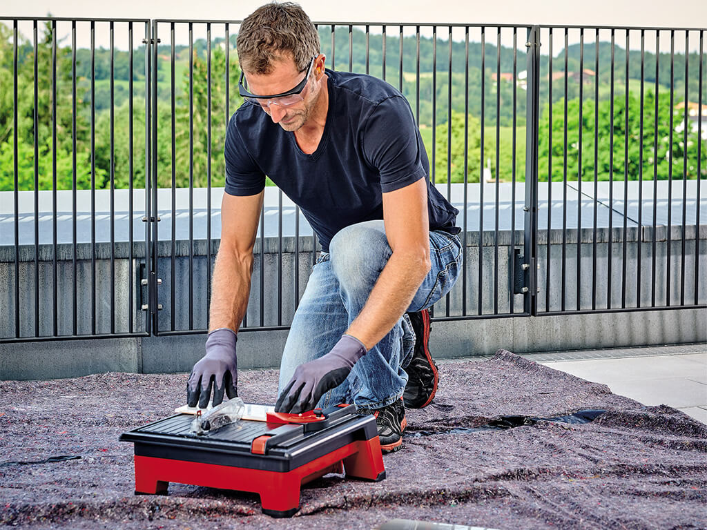 A man cuts a small tile outside on the balcony using the Einhell cordless tile cutter.