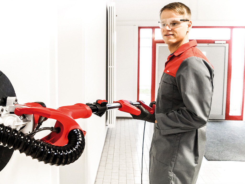 Man in protective clothing and goggles with drywall grinder