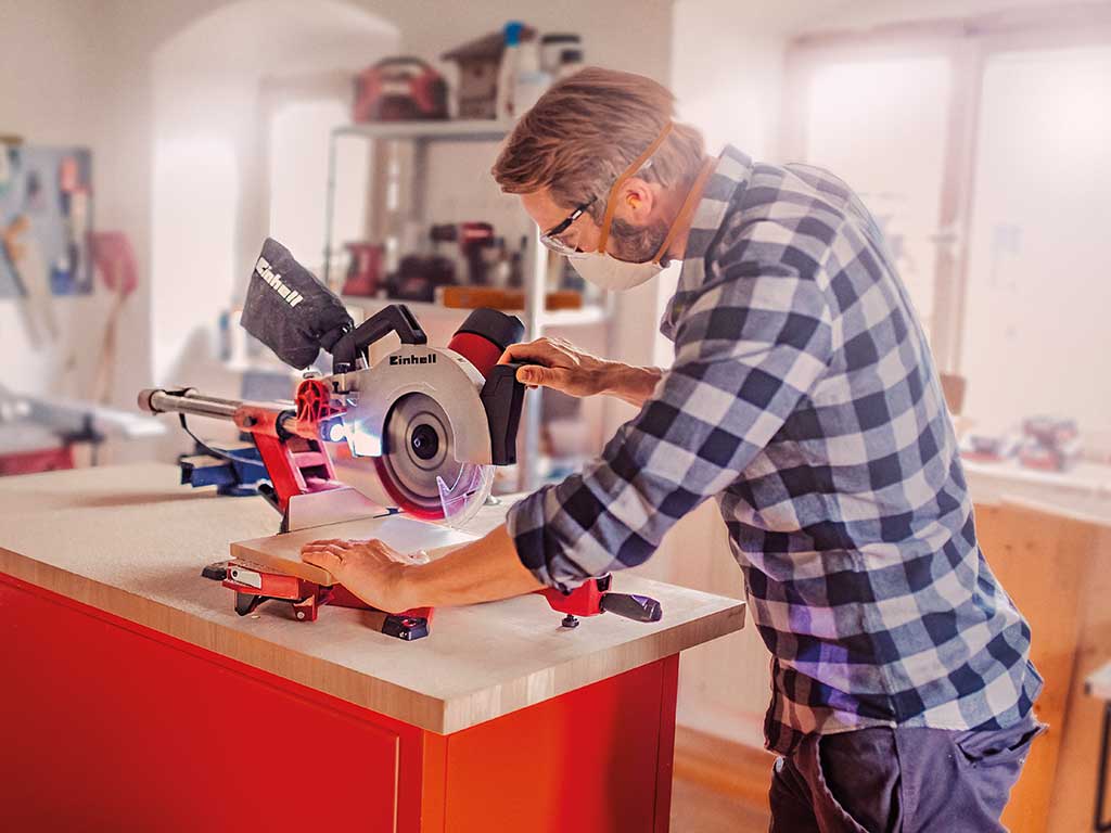 A man cutting wood with a mitre saw in his workshop.