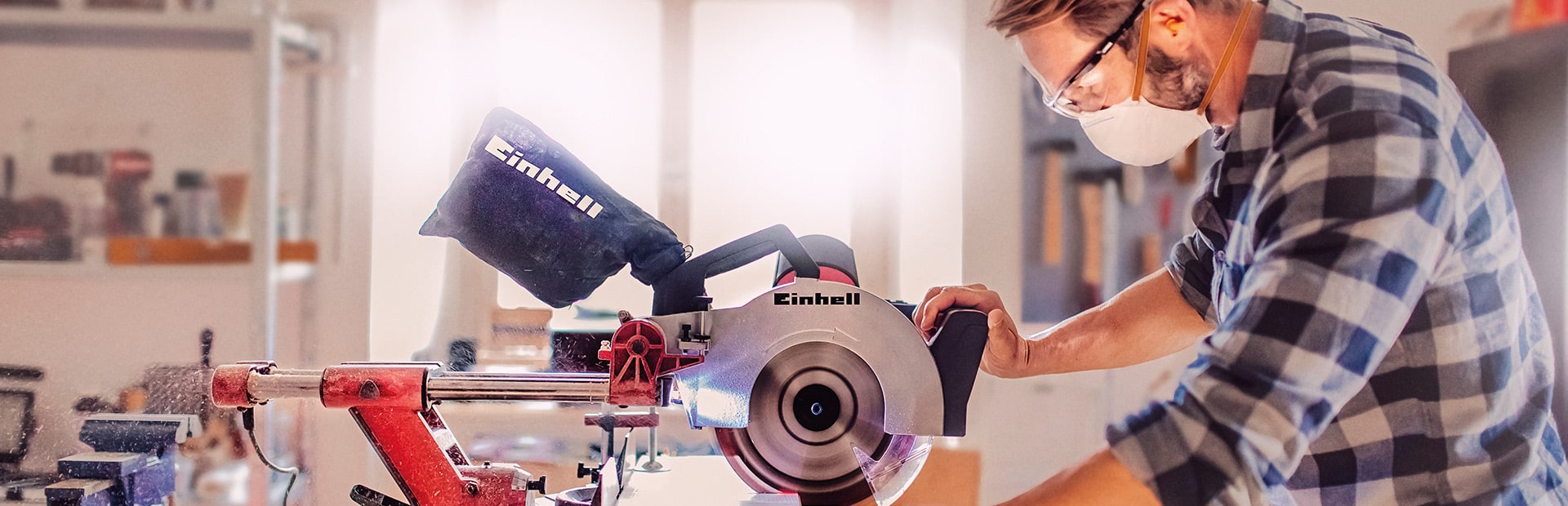 A man cuts a wooden board with an Einhell mitre saw in a workshop.