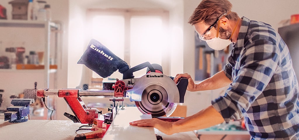A man cuts a wooden board with an Einhell mitre saw in a workshop.