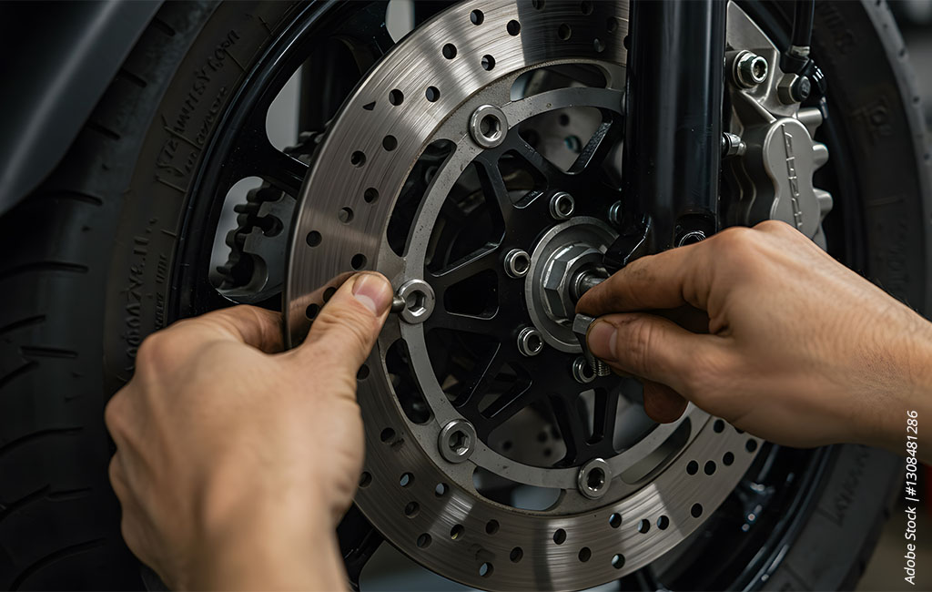 Hands checking the brake disc and wheel mounting on a motorcycle front wheel.