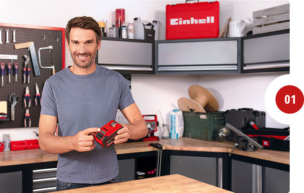 A man is holding the Einhell Multi-Ah battery and pointing to a button