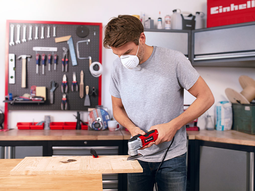 Man in his workshop using a multifunctional tool to sand a wooden board.