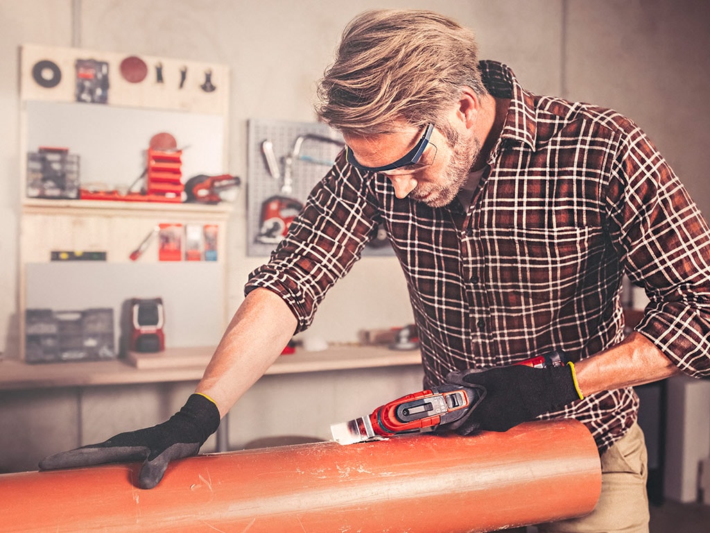 A man is cutting into a plastic pipe with a multifunctional tool.