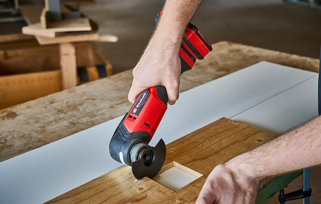 Nahaufnahme von Händen, die mit einem Einhell Akku Multitool eine Aussparung in einem Holzbrett ausschneiden.