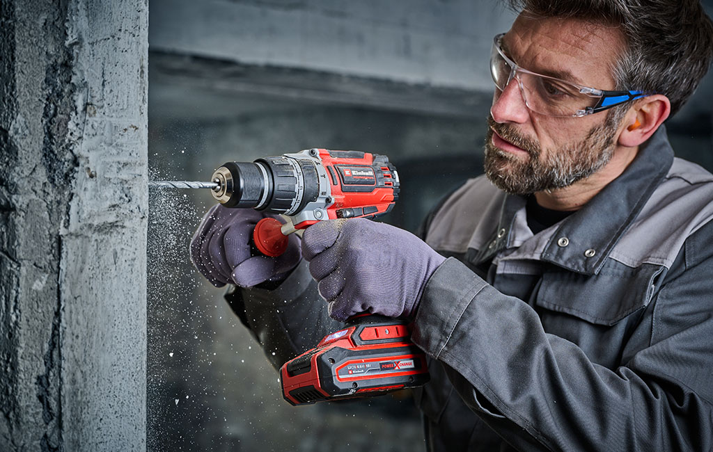 Mann bohrt mit einer Akku-Schlagbohrmaschine in Beton und trägt dabei Schutzbrille und Gehörschutz.