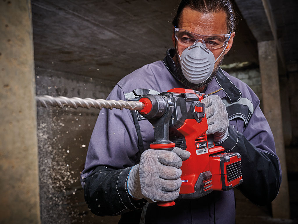 Mann bohrt mit einem Bohrhammer in Beton und trägt dabei Schutzbrille und Staubmaske.