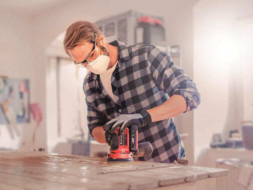A man sands wood with a rotating sander