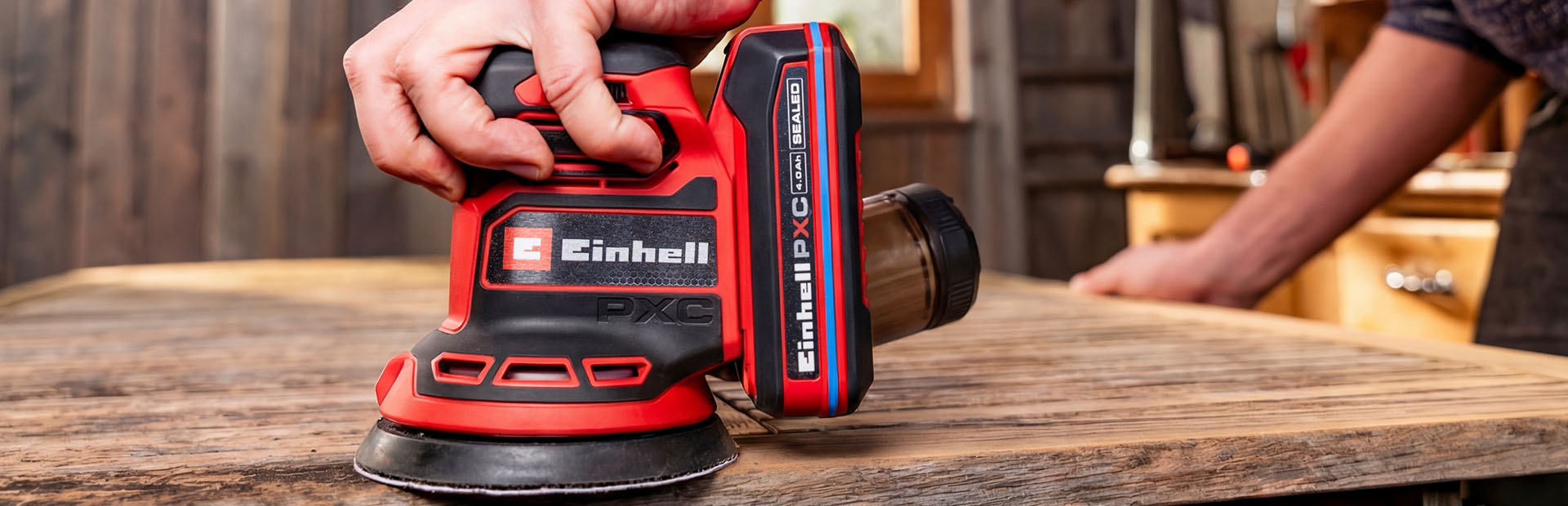 A man works on a wooden surface outdoors using a random orbital sander.