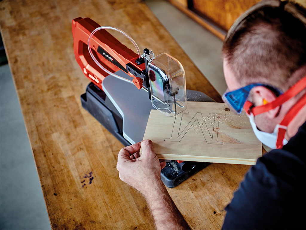 An M is cut from a wooden board with a scroll saw