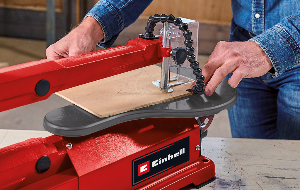 A man is cutting a shape out of a thin wooden board using the Einhell scroll saw.