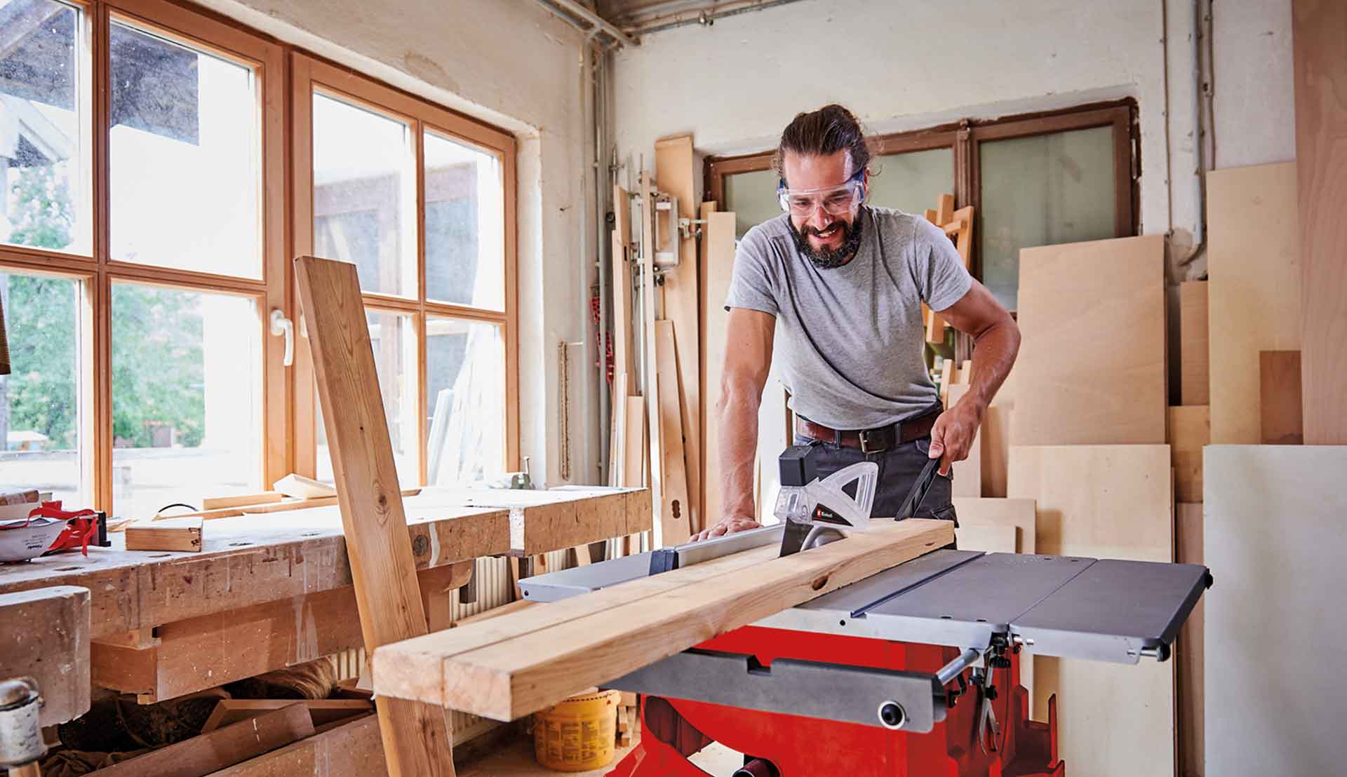 Ein Mann sägt eine lange Holzlatte mit Hilfe einer Tischkreissäge zu.