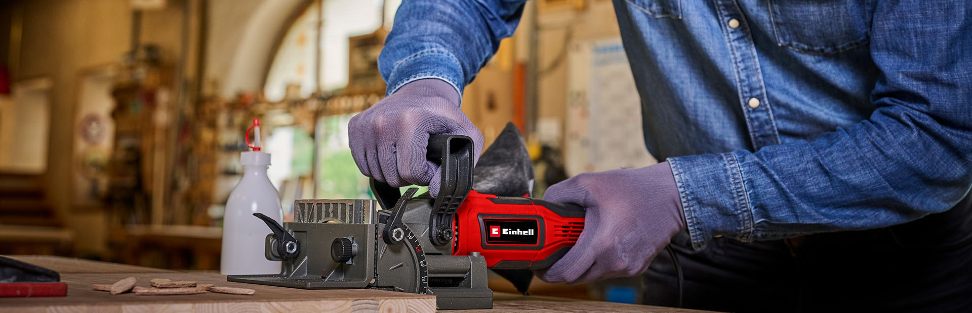 Close-up of a cordless Einhell biscuit joiner cutting a slot into a clamped wooden board.