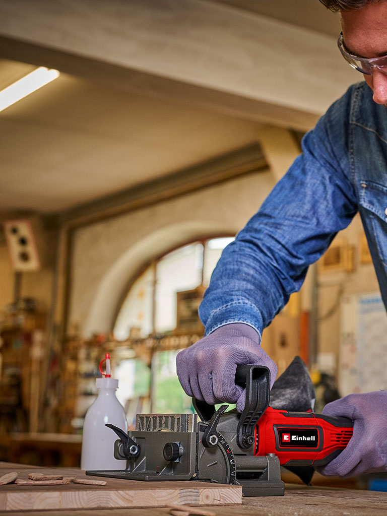 Close-up of a cordless Einhell biscuit joiner cutting a slot into a clamped wooden board.
