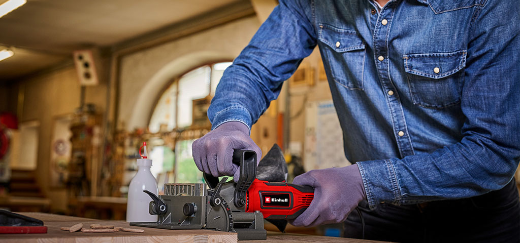 Close-up of a cordless Einhell biscuit joiner cutting a slot into a clamped wooden board.