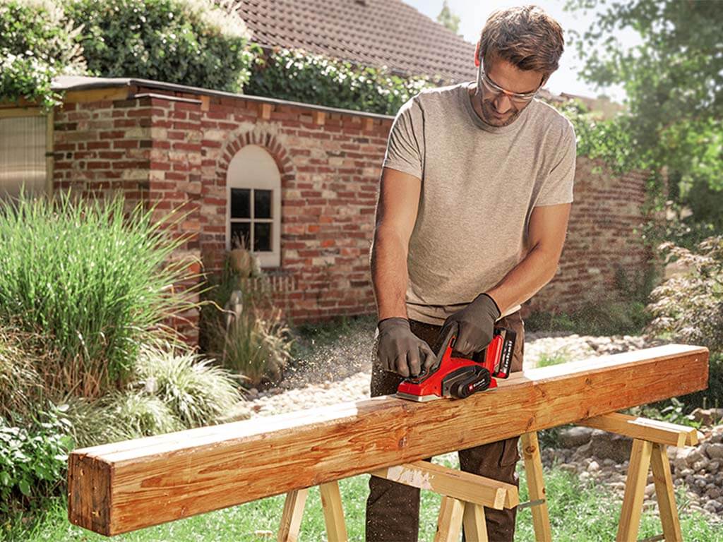 a man works wooden beams with planing machine 