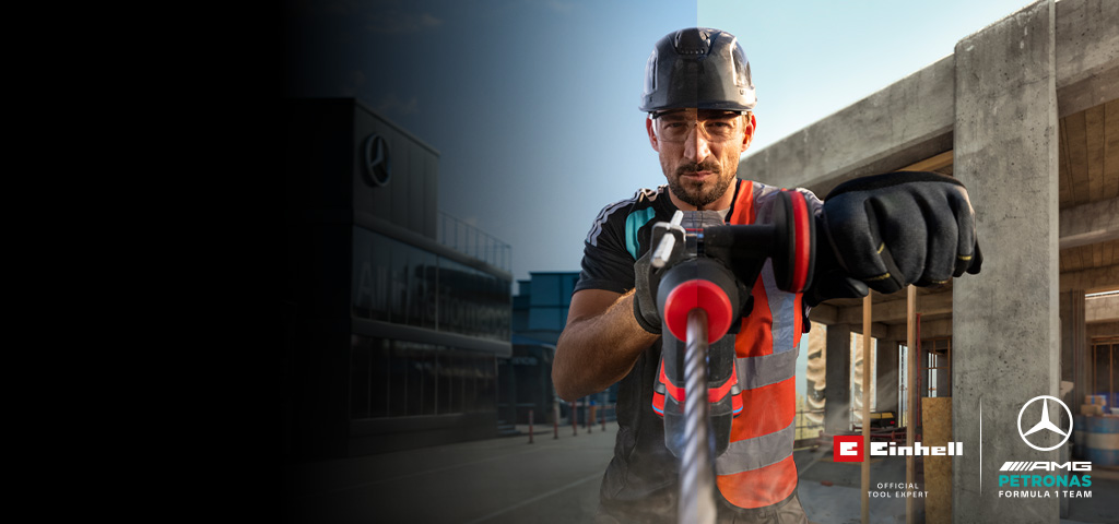 A mechanic in protective gear drilling with a power tool at a construction site.