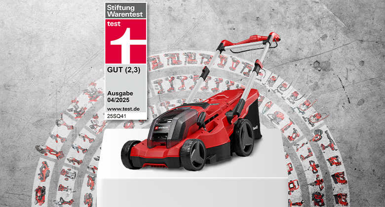 An Einhell cordless lawn mower GP-CM 36/450 on a white pedestal in front of a concrete wall. On the left, a Stiftung Warentest test label: GOOD (2.3), issue 04/2025, 25SQ41. In the background, many compatible Power X-Change tools are arranged in a circular pattern.
