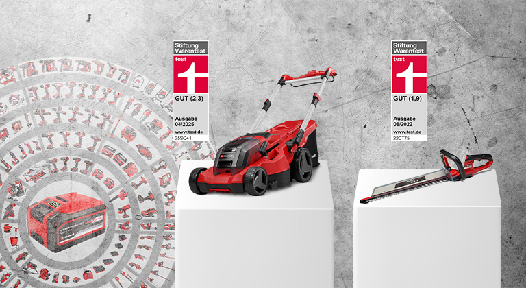 An Einhell cordless lawn mower and cordless hedge trimmer on white pedestals in front of a concrete wall. To the left, a Power X-Change battery with icons of compatible tools. The lawn mower was rated GOOD (2.3) by Stiftung Warentest, issue 04/2025. The hedge trimmer was rated GOOD (1.9), issue 08/2022.