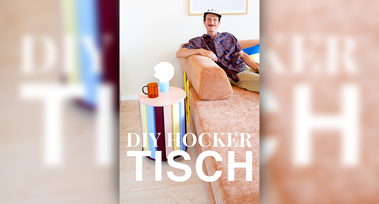 Ein Mann sitzt auf einem lachsfarbenen Sofa neben einem bunten, zylindrischen Beistelltisch mit dem Text „DIY HOCKER TISCH“.