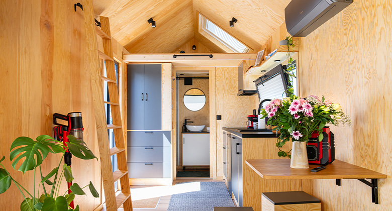 Blick in den hellen Innenraum eines Tiny Houses mit Holzverkleidung, Leiter zur Empore, Küchenzeile und Esstisch.