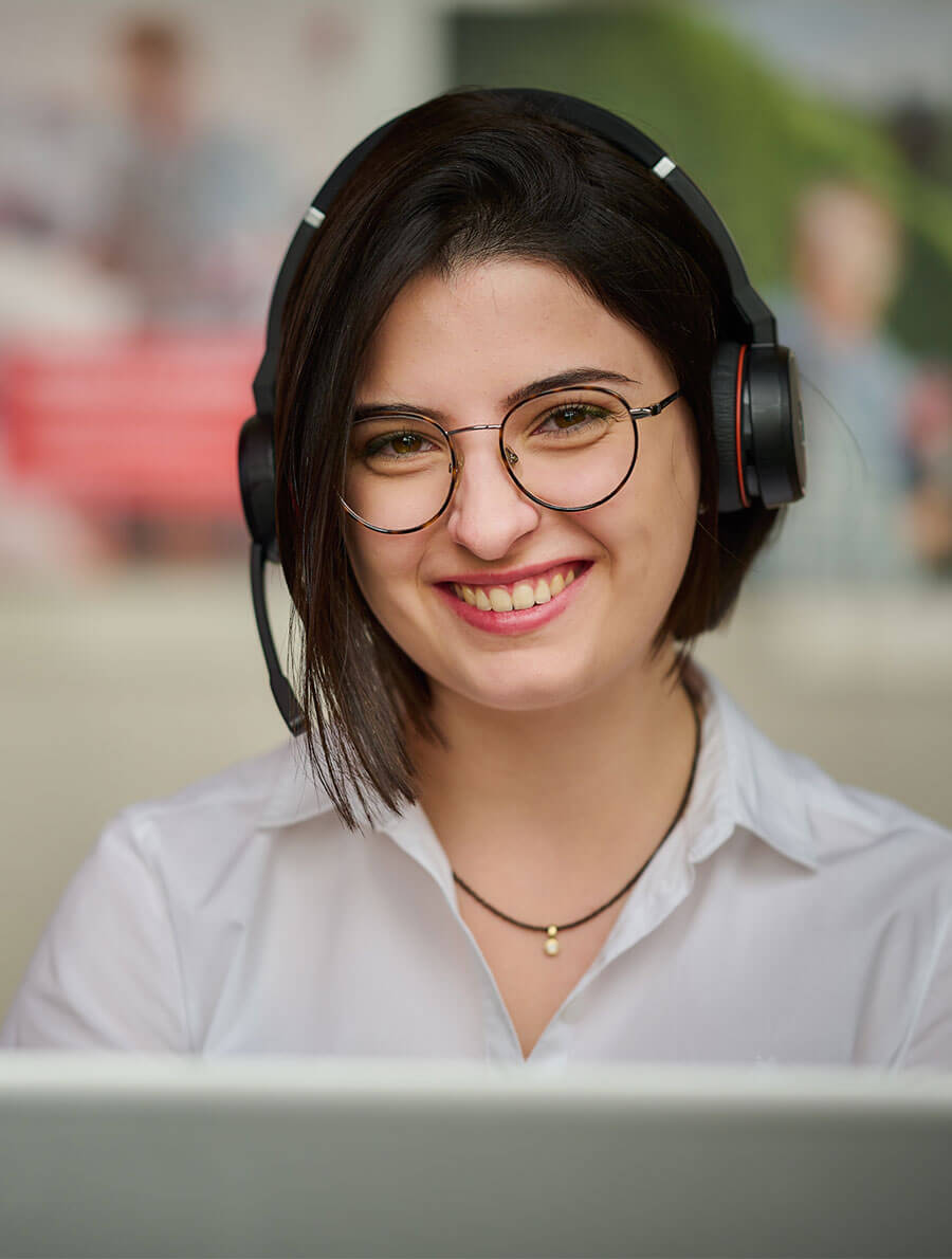 A woman is sitting in front of her laptop and smiles at the camera.