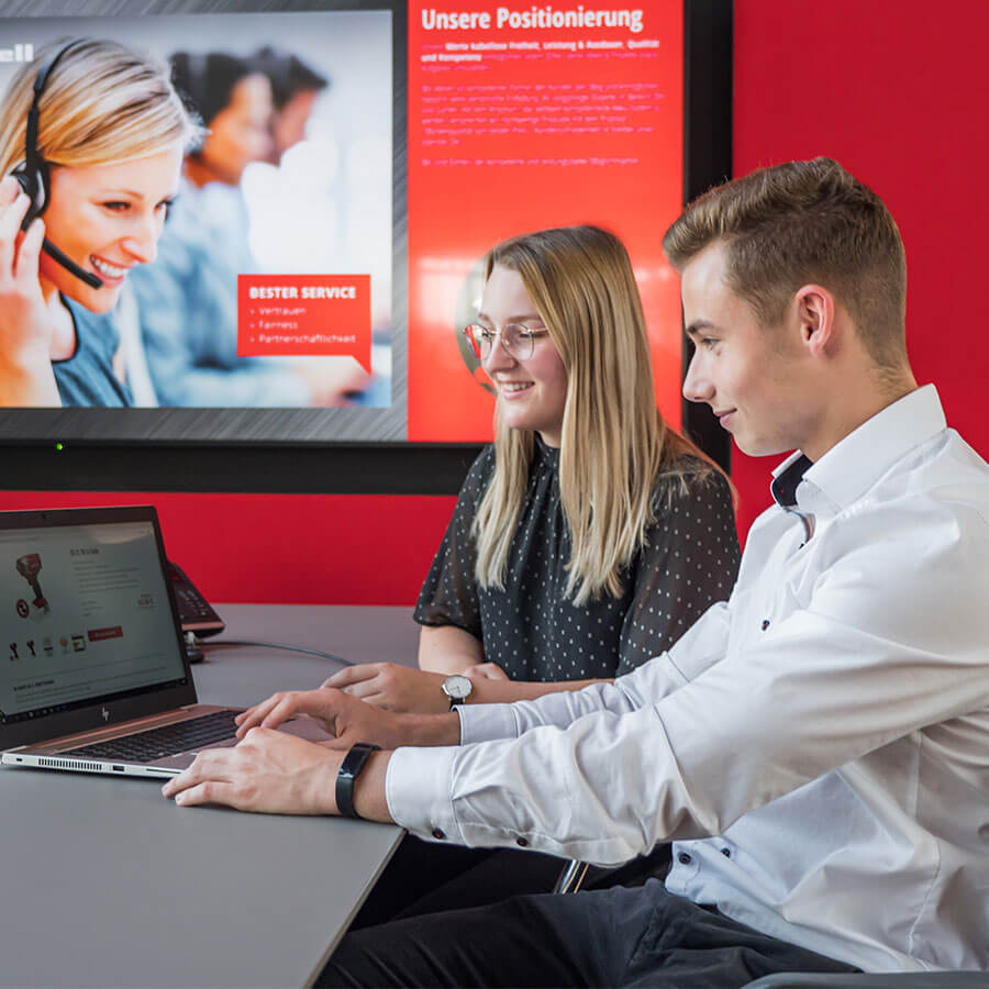 A man and a woman are sitting in a meeting room and are both looking into the computer.