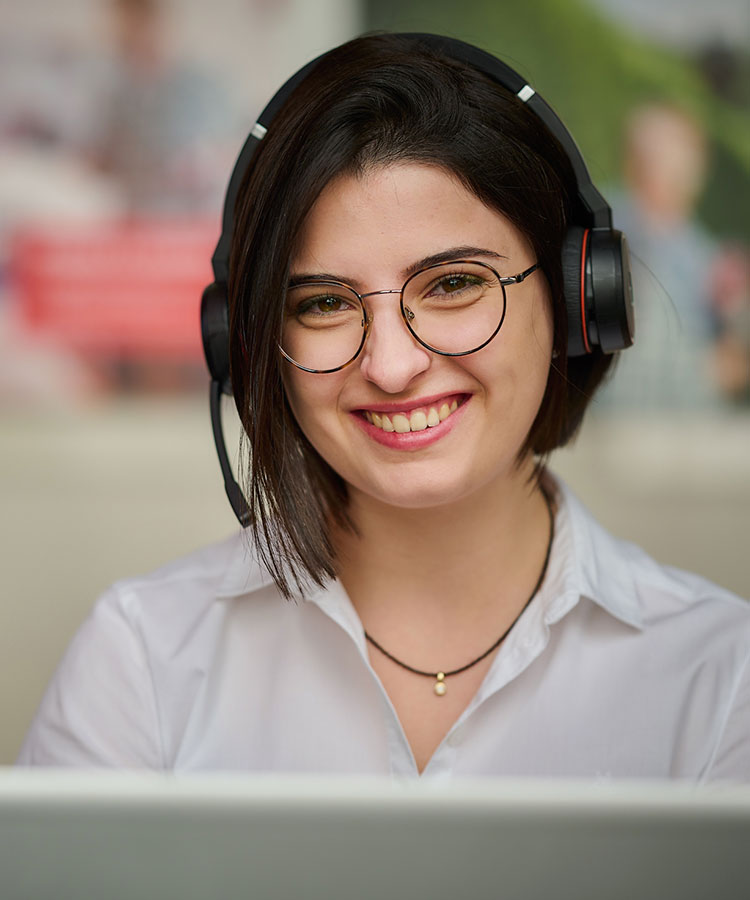 a woman with a headset sits laughing in front of her laptop
