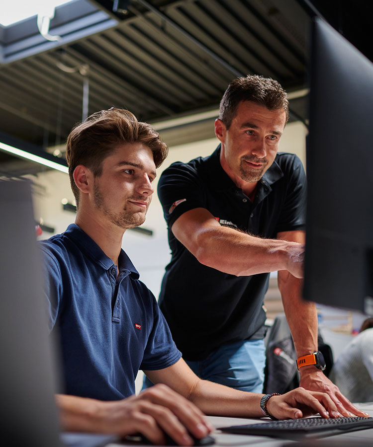 a boy sits at the computer while a man explains something to him