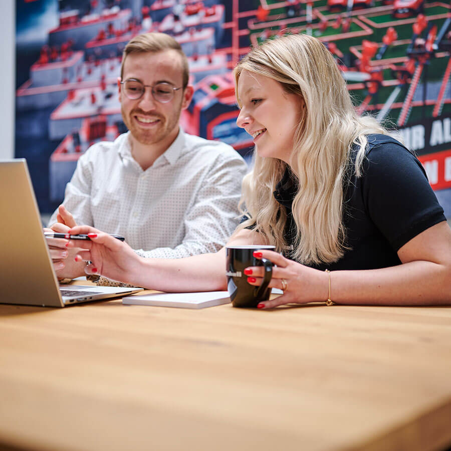 a woman and a man sit laughing in front of a computer