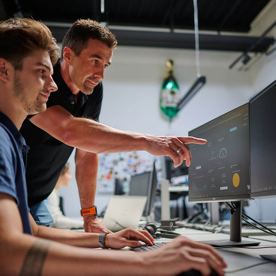 a boy is sitting at the computer and a man is explaining something to him