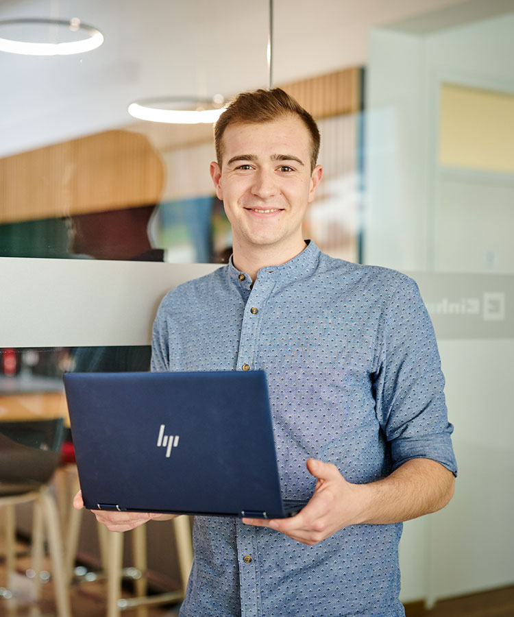 a man smilingly holds a laptop in his hand
