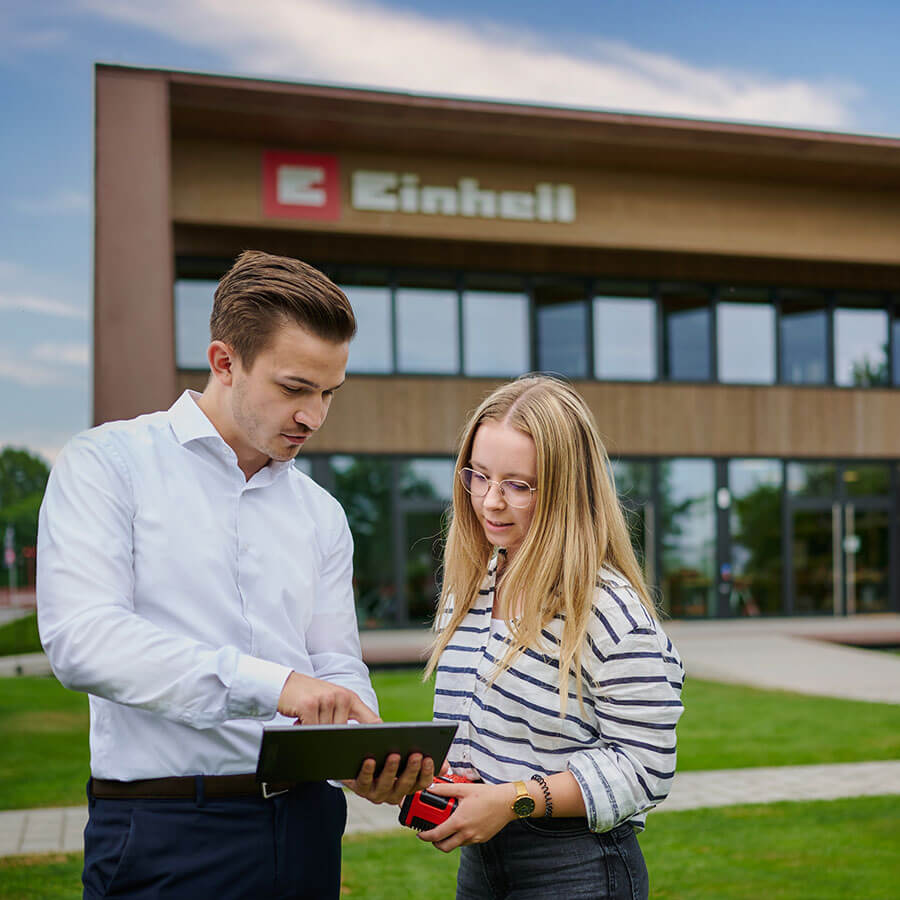a man explains something on the tablet to a woman who is holding a battery in her hand