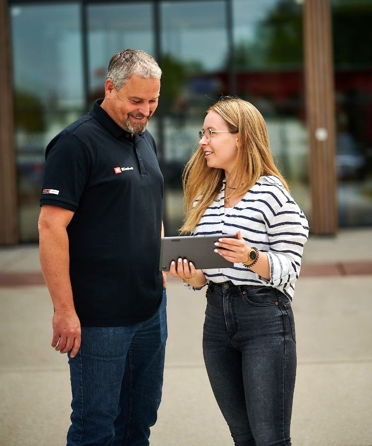 A man and a woman standing in front of the Einhell Welt and looking at the laptop.