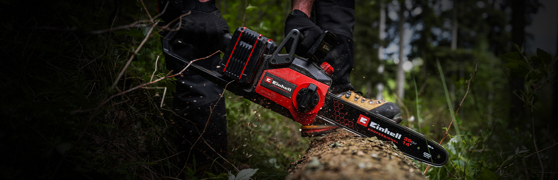 Ein Mann sägt mit einer Einhell Akku-Kettensäge einen Baumstamm im Wald.