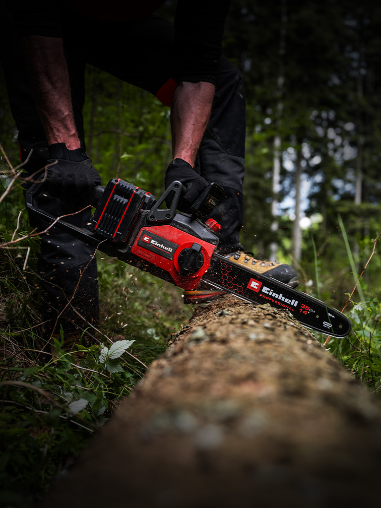 Ein Mann sägt mit einer Einhell Akku-Kettensäge einen Baumstamm im Wald.