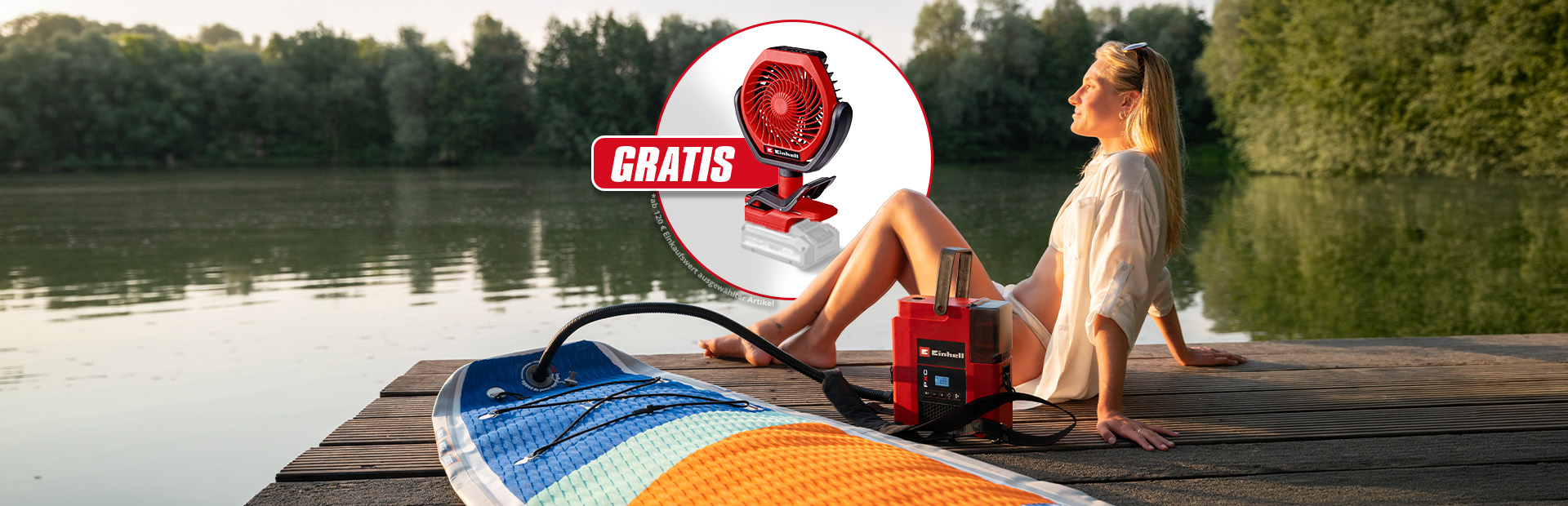 Frau sitzt am See auf Steg, rotes Einhell Gerät pumpt SUP auf, Einblendung mit Ventilator und Text „GRATIS“.