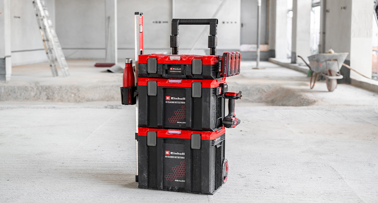 Two stacked Einhell E-Case tool cases with telescopic handle and accessories like a water bottle and holder on a construction floor.