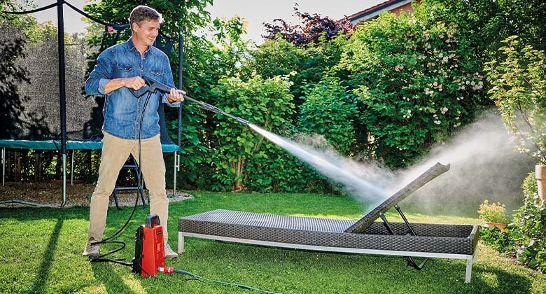 Mann reinigt Gartenliege mit einem Hochdruckreiniger