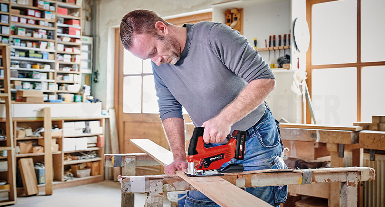 Mann in einer Werkstatt, der mit einer Stichsäge Holz zersägt
