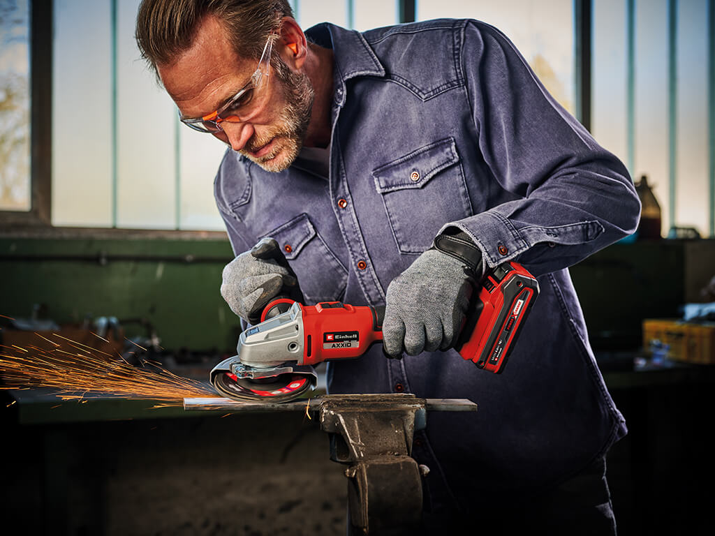 A man wearing safety goggles and protective gloves works with an angle grinder