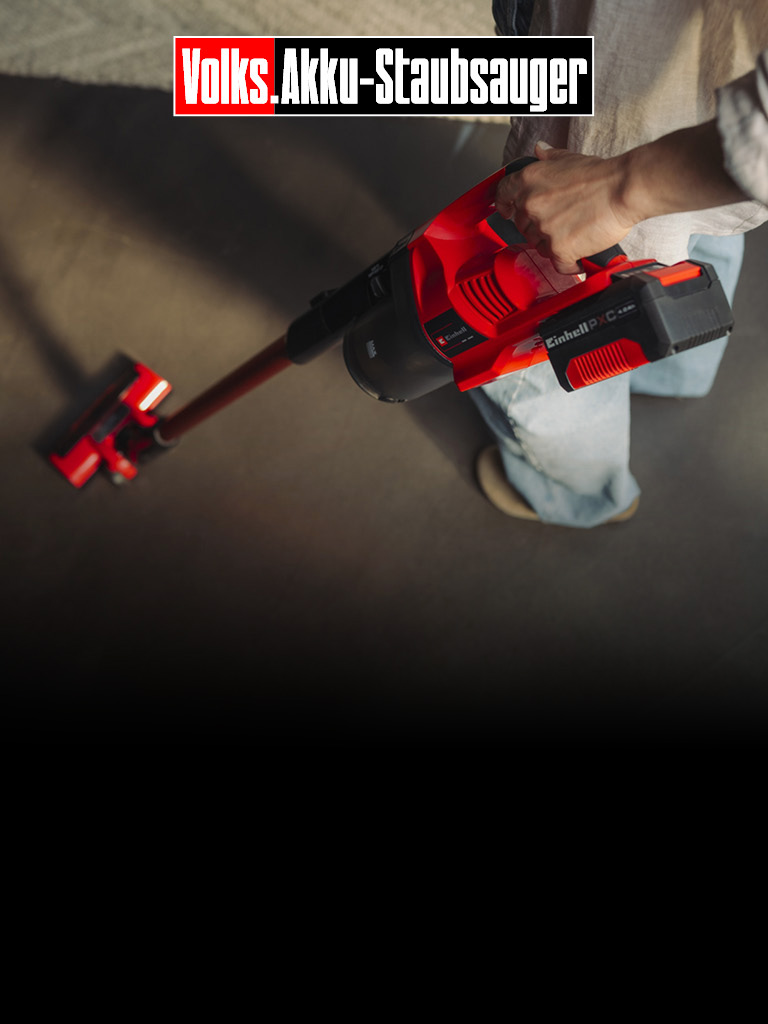 Das Bild zeigt eine Person, die einen roten kabellosen Stabstaubsauger auf einem Boden benutzt. Sichtbares Branding und Text lauten „Volks Akku‑Staubsauger“ und „Einhell“, was auf einen akkubetriebenen Staubsauger hinweist.