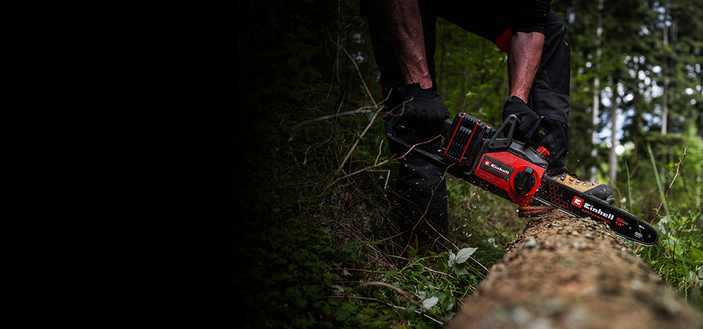 ChatGPT said: A person is using a red-and-black cordless chainsaw to cut through a fallen tree in a dense forest. The scene shows wood chips flying as the saw cuts into the trunk.